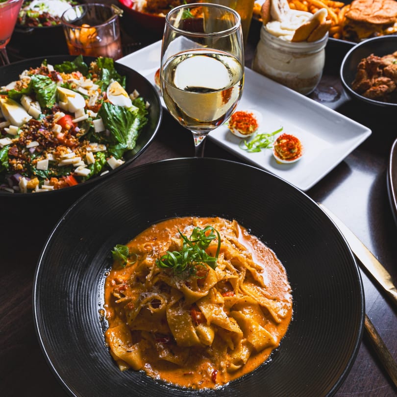Southern-style pasta with red sauce, salad, deviled eggs, and white wine on a dark table.