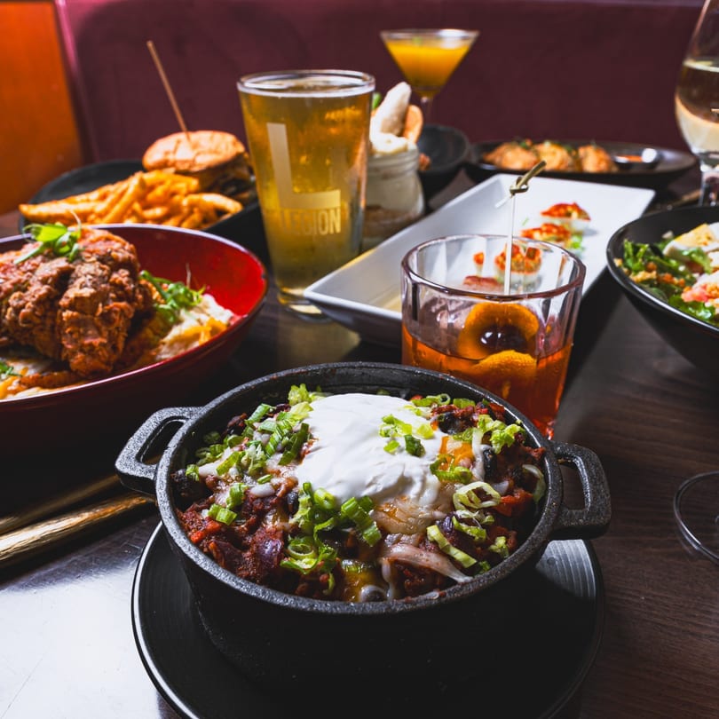 A table laden with Southern dishes including chili, fried chicken, burgers, fries, and cocktails.