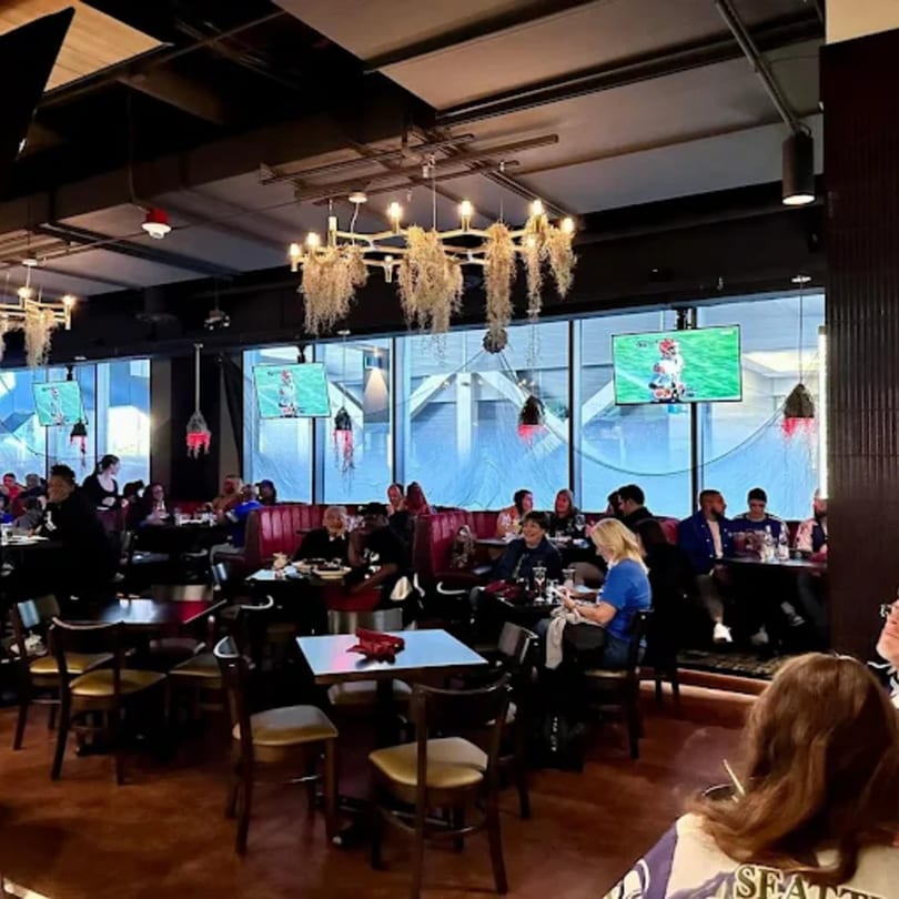 Legion Sports Bar interior with patrons dining, watching sports on multiple screens, and modern chandeliers.