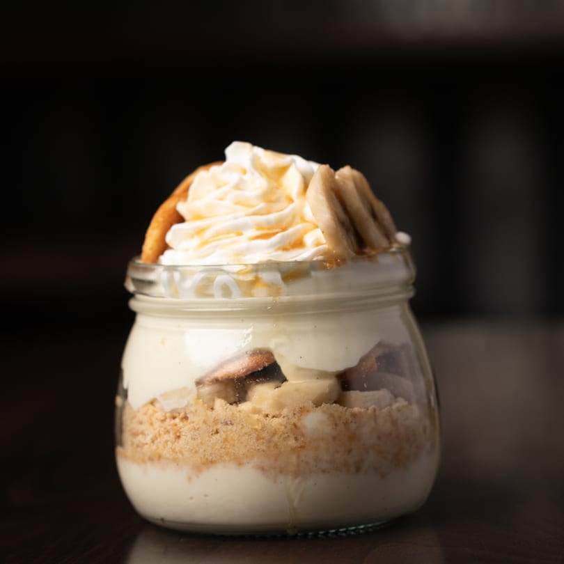 Southern banana pudding in a jar, topped with whipped cream, caramel, and vanilla wafers.