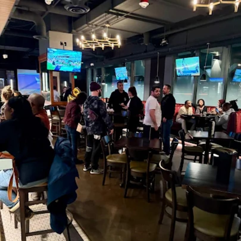 Legion Sports Bar interior with patrons standing and sitting, multiple TVs showing sports, and modern lighting.