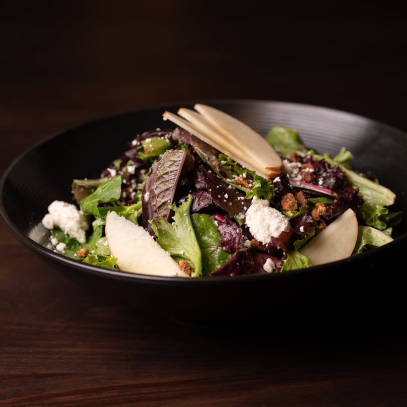 A fresh Legion Sports Bar salad with mixed greens, goat cheese, candied pecans, and sliced pears.